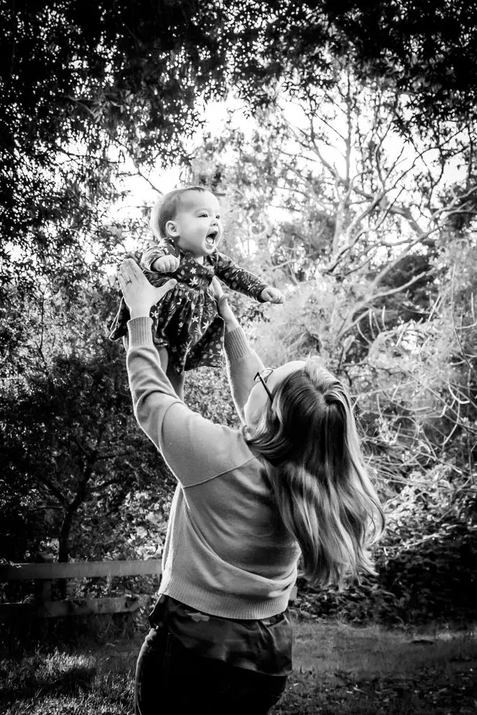 Mom lifting laughing baby high above head in black and white family portrait