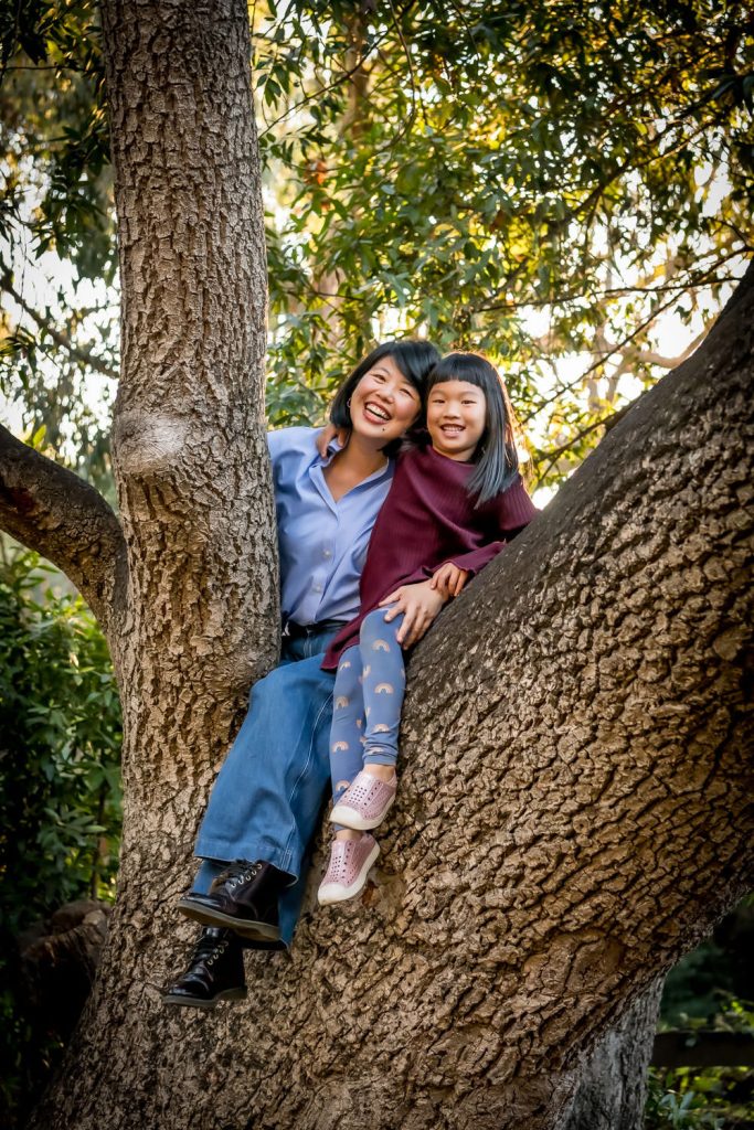 Mother and daughter sitting in tree laughing for family portrait by photographerShelly Rivoli